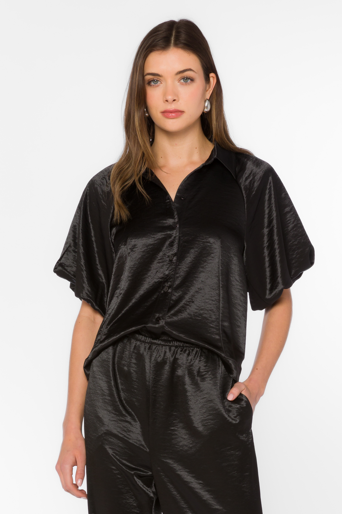 Woman wearing the Stephanie Top, a black satin button-front blouse with short dolman sleeves.