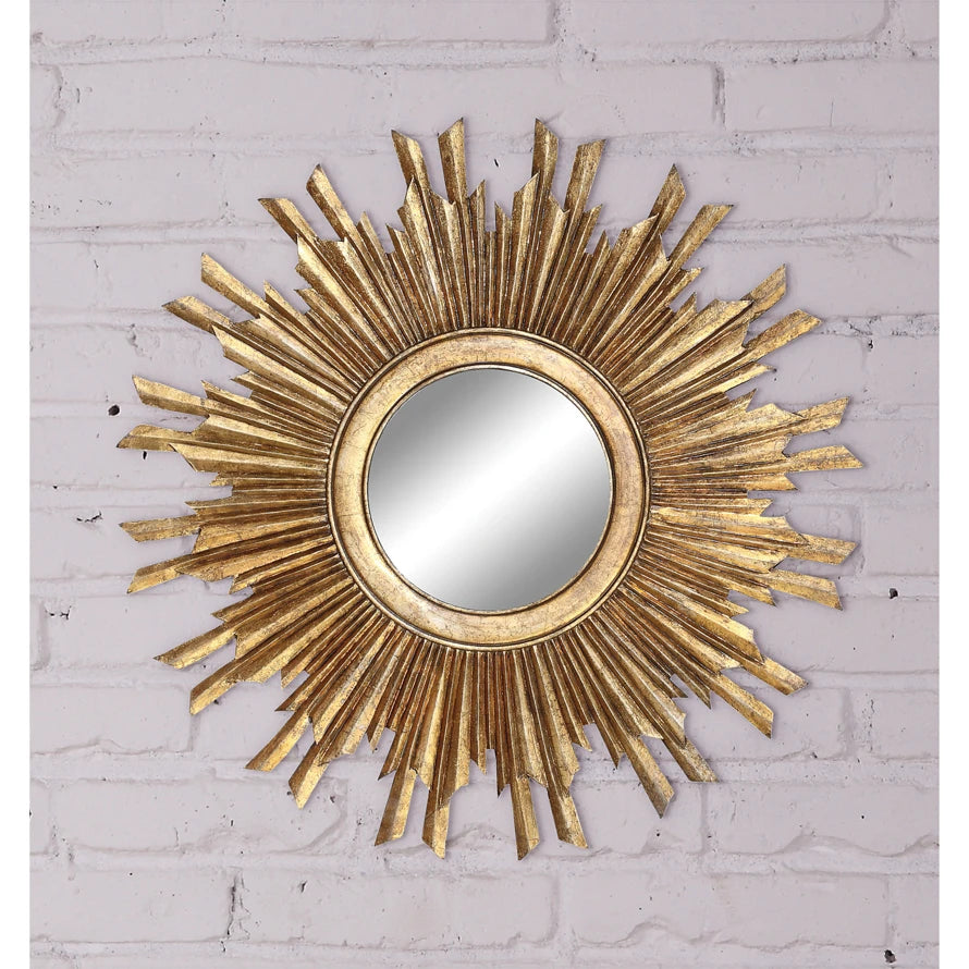 Round sunburst wall mirror with a gilded gold wood frame on a white brick wall.