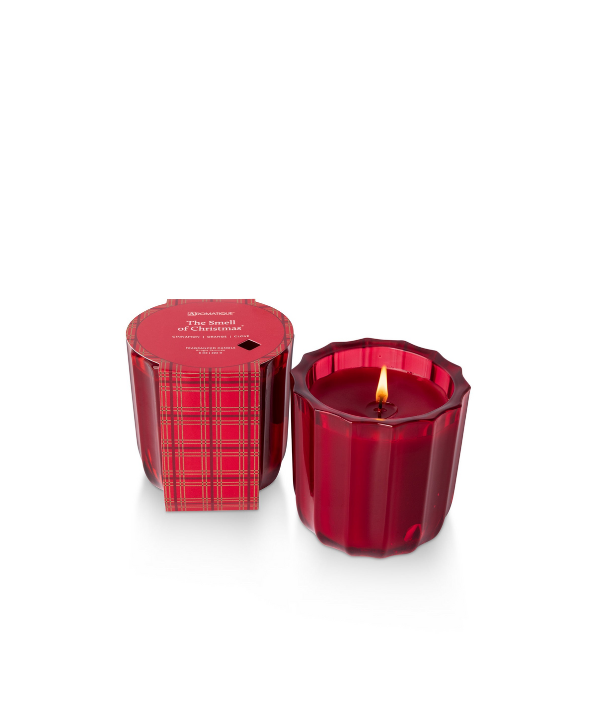 The Smell of Christmas candle in a red ribbed glass vessel with a plaid wrap and lit wick.