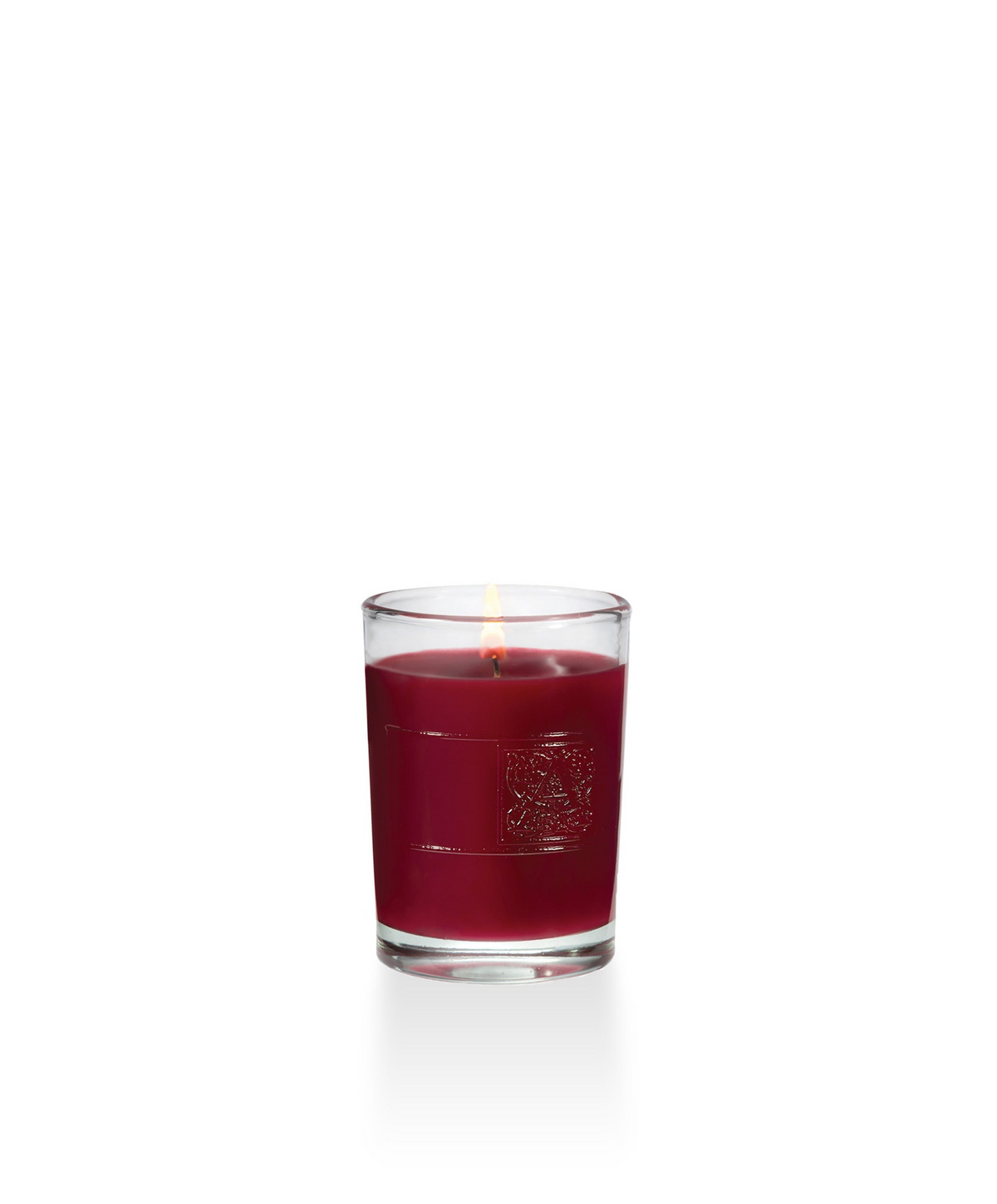 The Smell of Christmas Votive Glass Candle with red wax and a lit wick in a clear glass container.