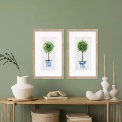 Two framed prints of rosemary topiary in blue and white pots on a green wall.