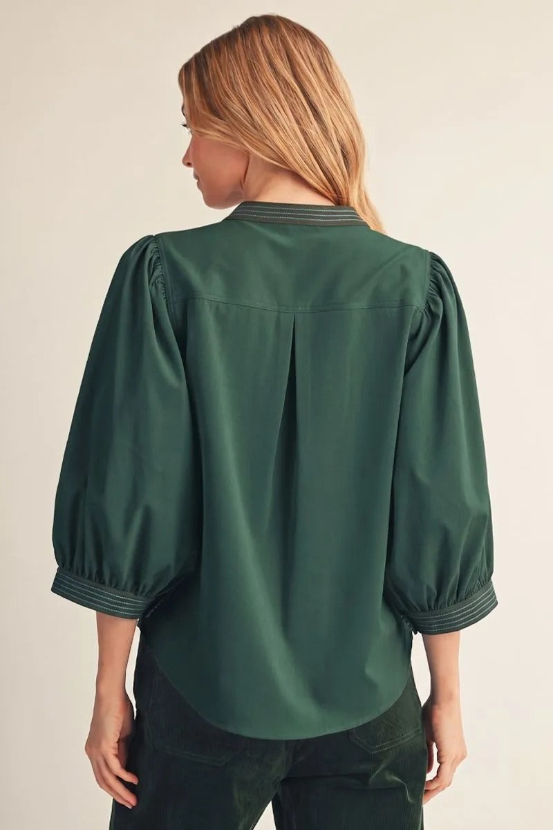 Back view of a woman wearing a dark green Trixie solid top with puff sleeves and a pleated back.