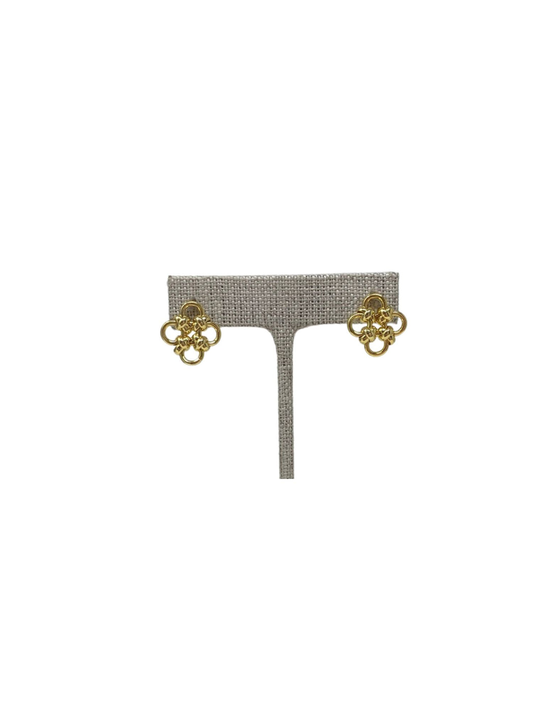 A pair of gold polished woven quatrefoil stud earrings displayed on a grey textured stand.