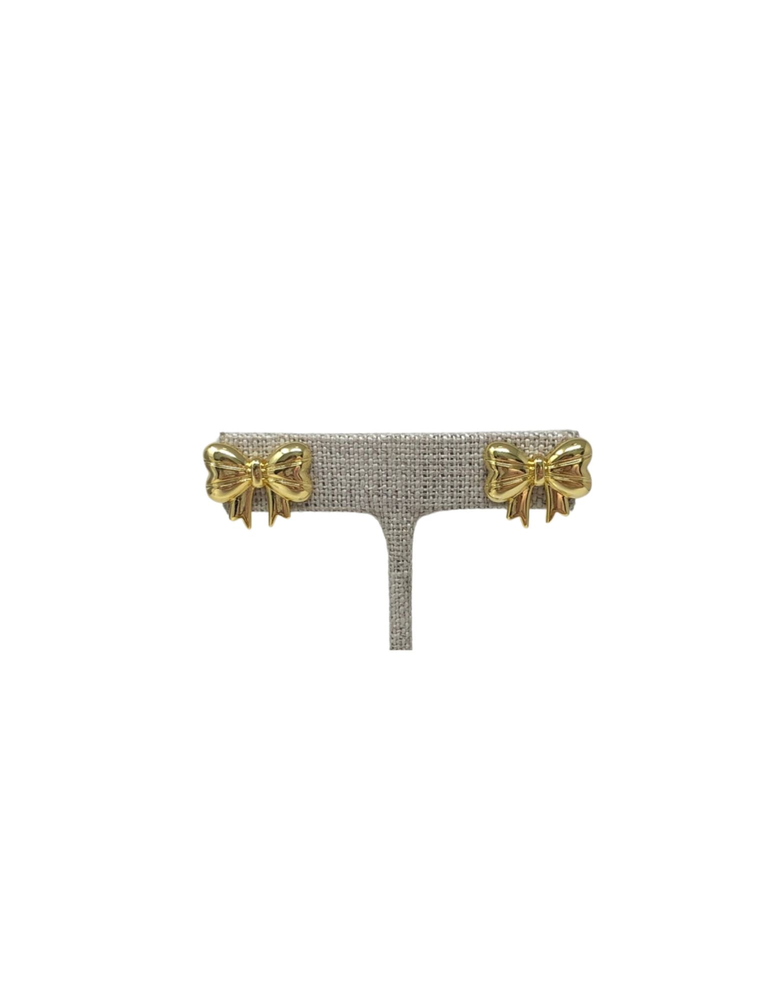 Pair of gold polished classic bow-shaped stud earrings on a grey display stand.