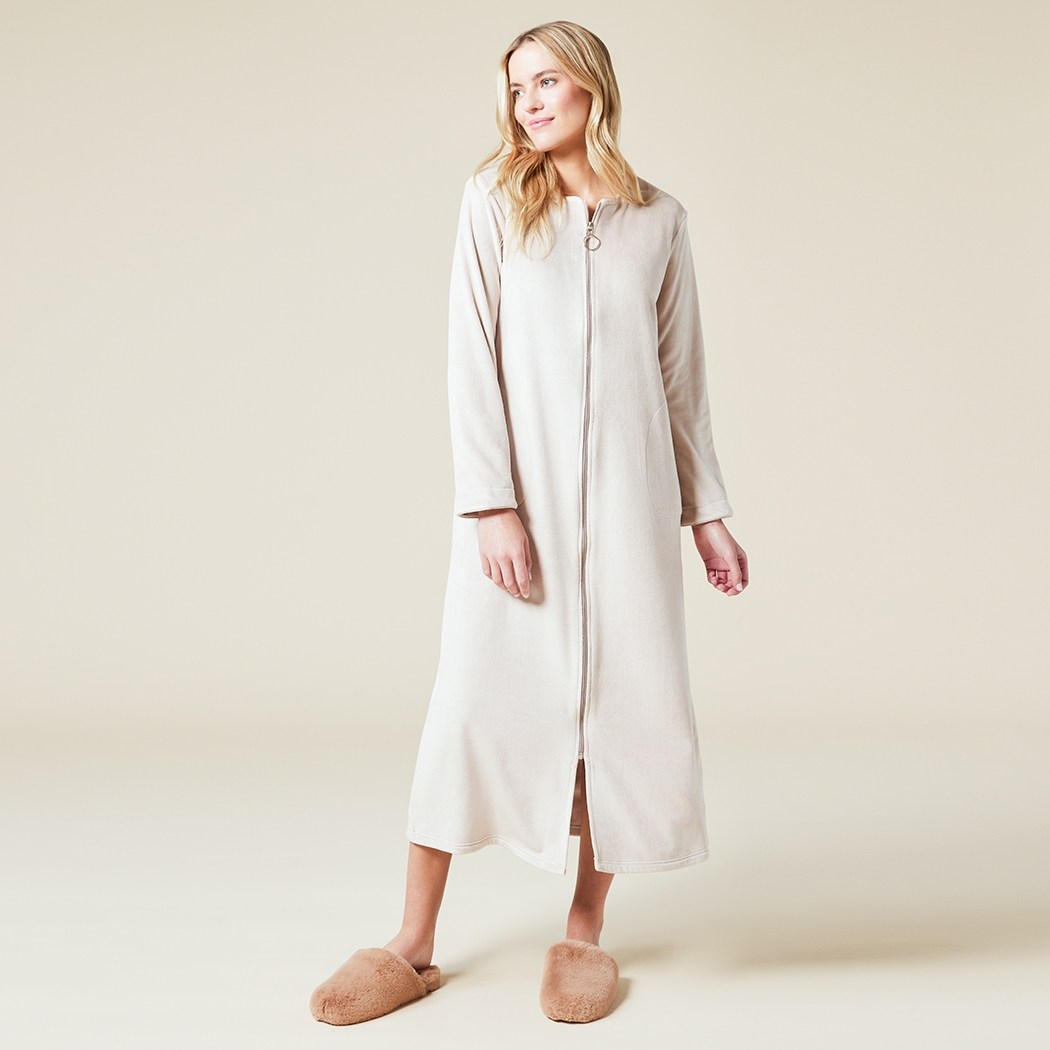 Woman wearing a full-length cream-colored soft zip robe with a sweetheart neckline and slippers.