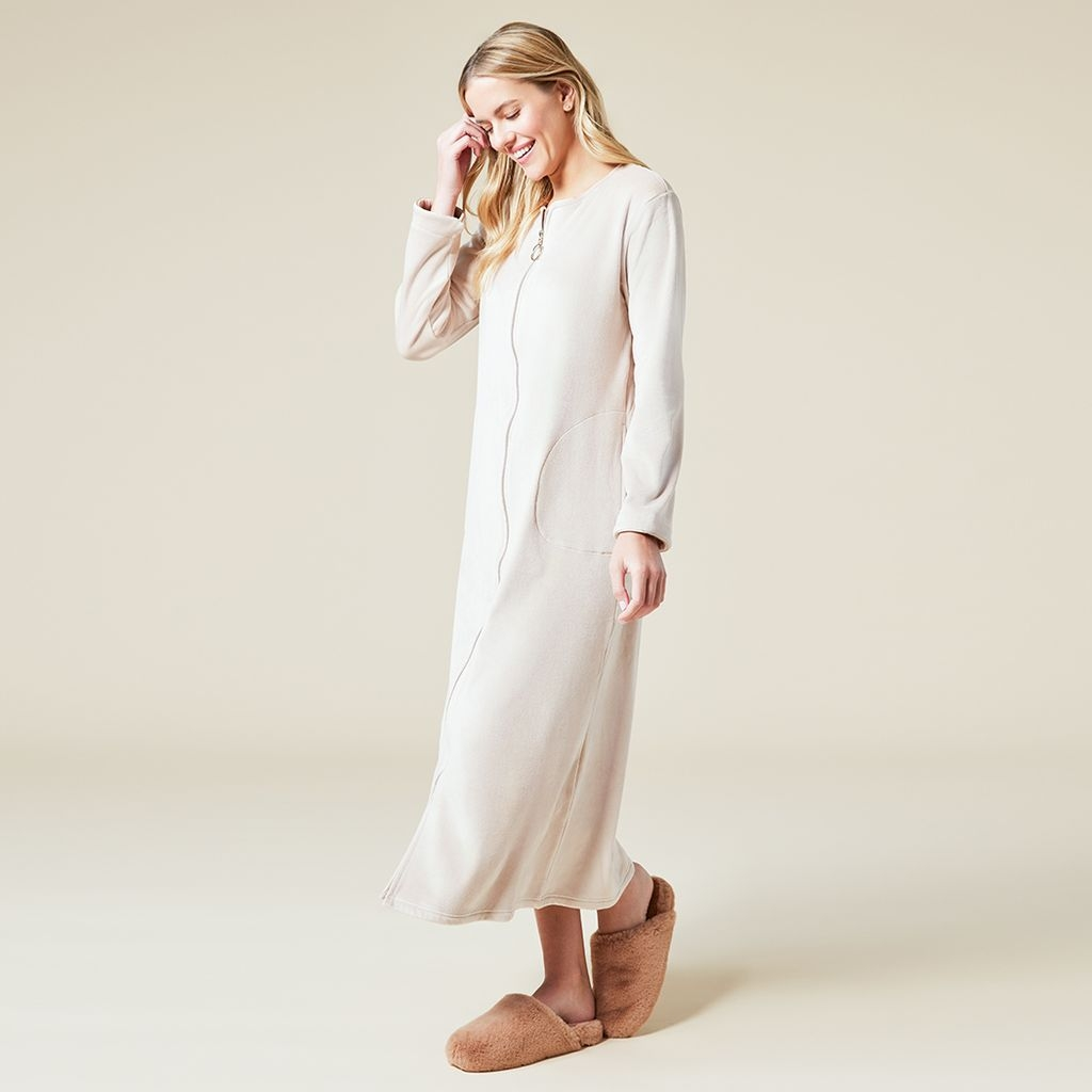 Woman wearing a full-length cream-colored soft zip robe with side pockets and fuzzy slippers.