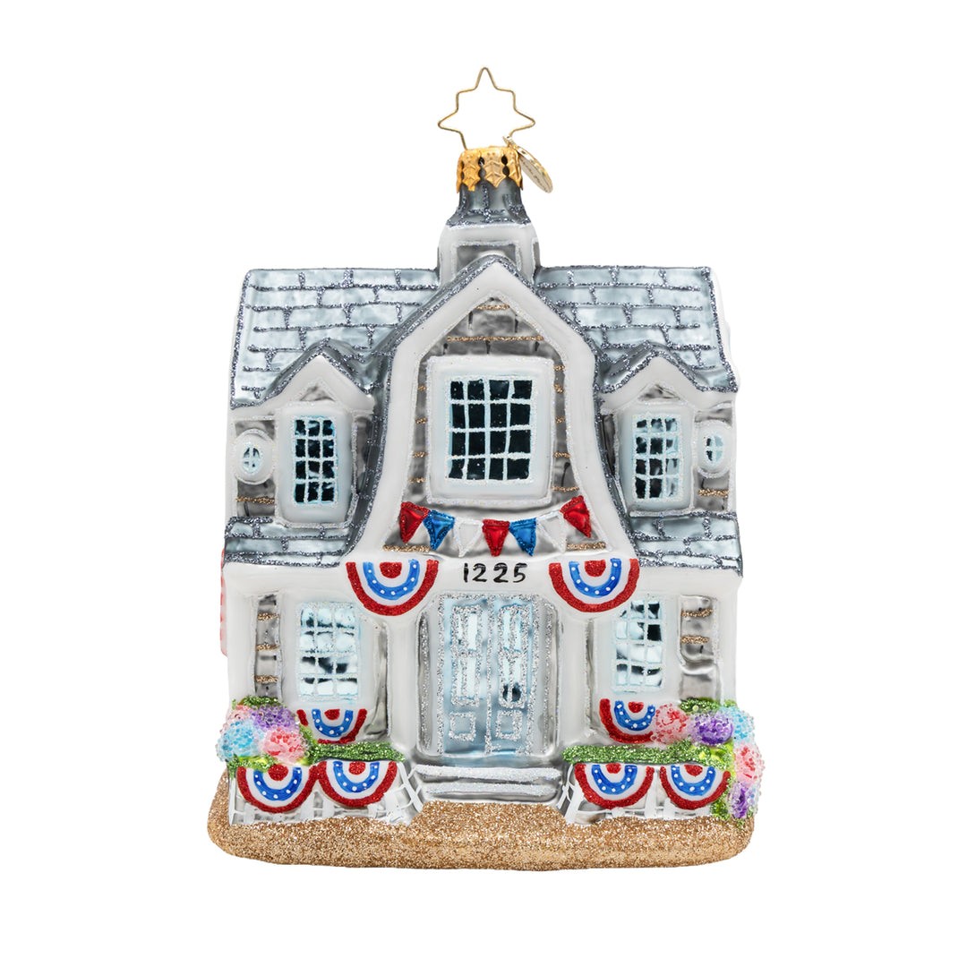 Glass New England beach house ornament with patriotic bunting and a glittery base.
