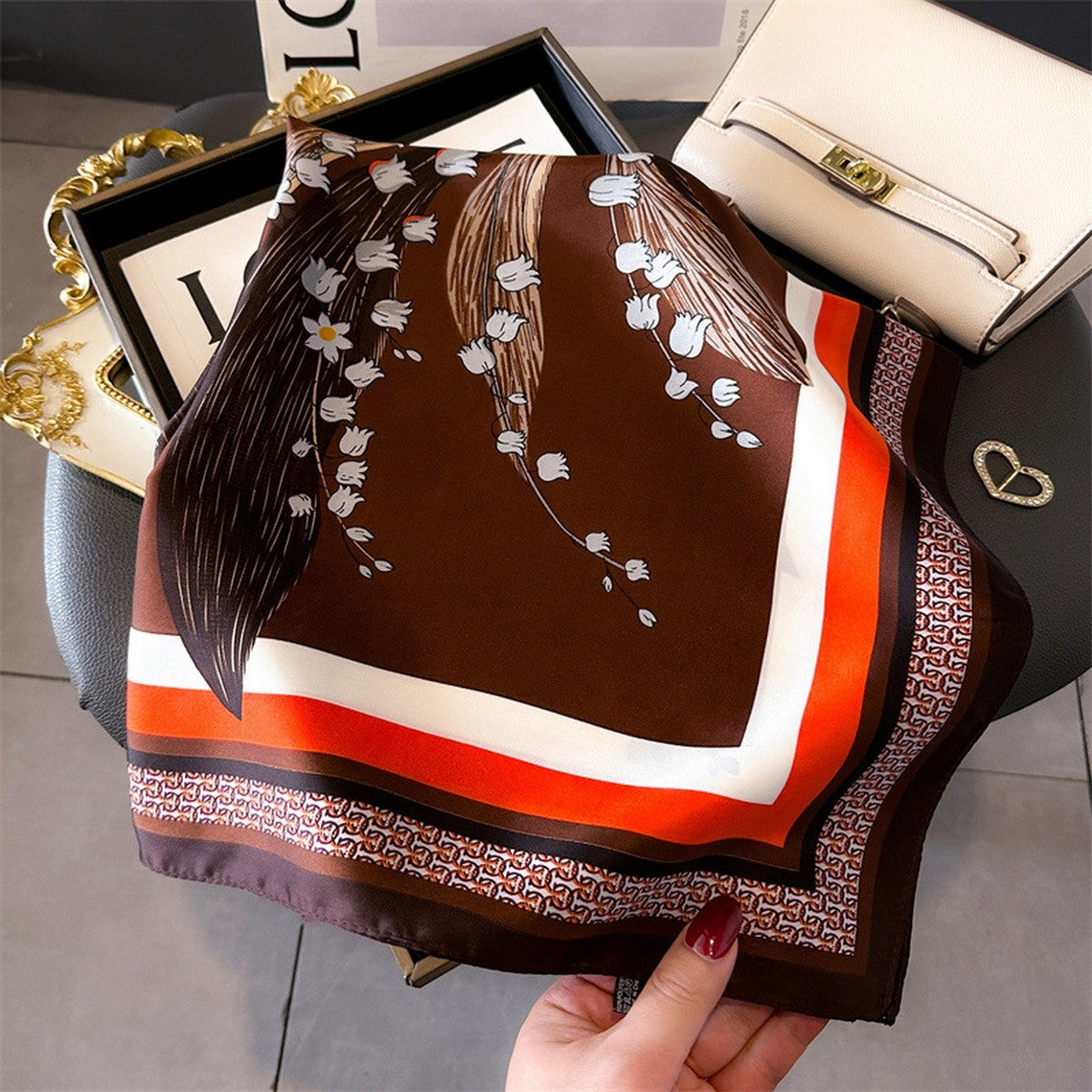 Artistic printed small square scarf in brown with white floral patterns and orange border accents.
