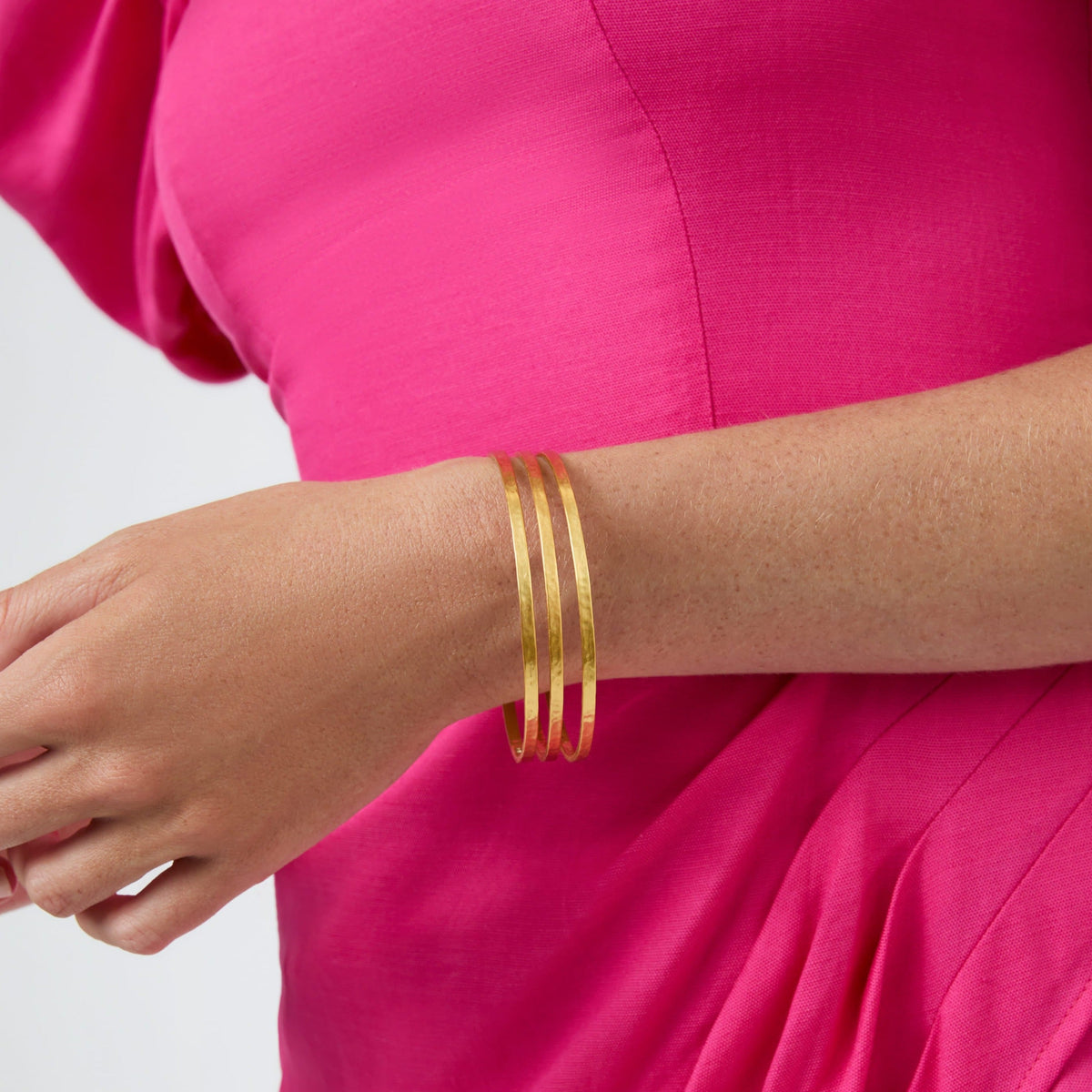 A person wearing three thin, hammered 24K gold-plated Crescent Bangles on their wrist.