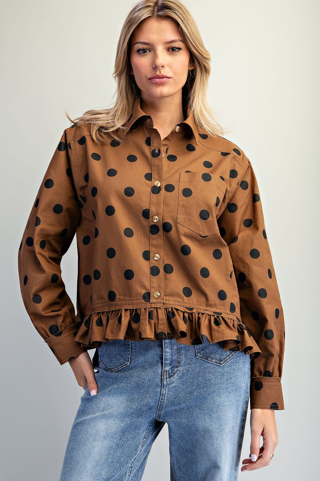 Woman wearing a brown polka dot button-down blouse with a ruffled hem and blue jeans.