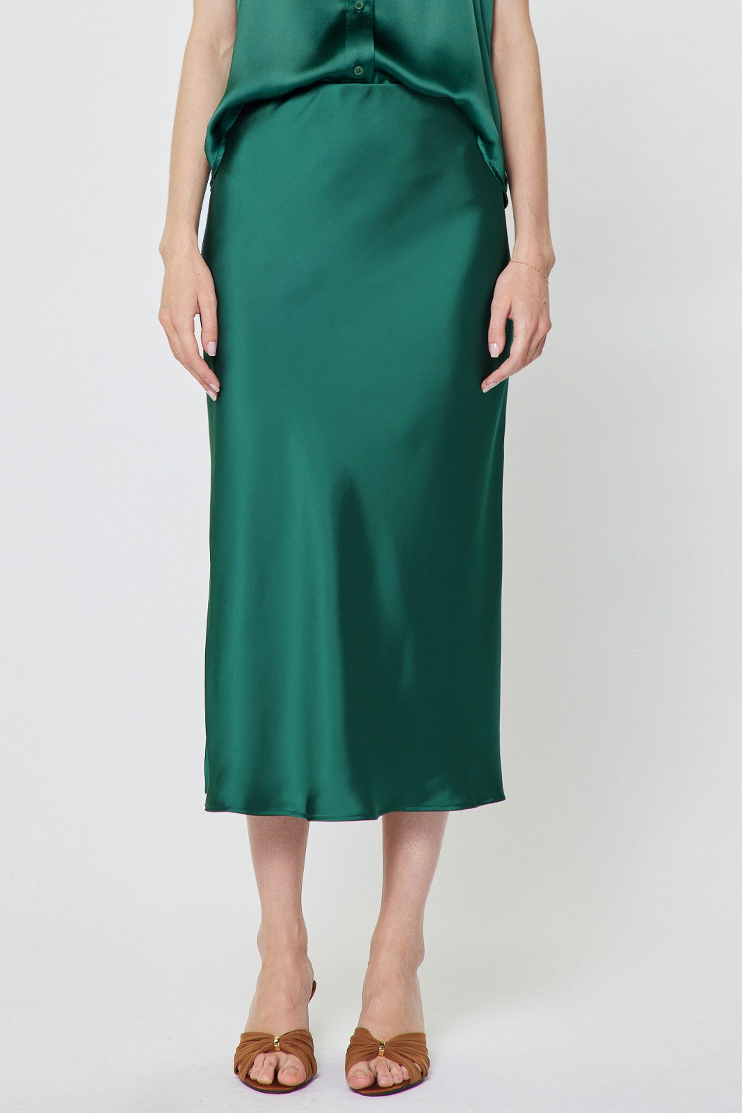 A woman wearing a green satin Loisa midi skirt with an elasticized waist and bias cut.