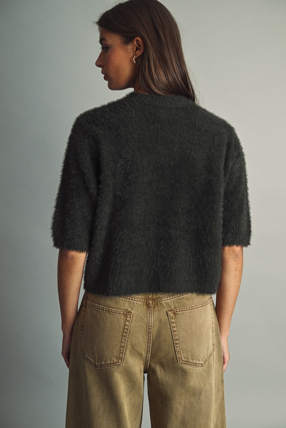 Back view of a woman wearing a dark brown fluffy cropped faux-fur sweater and tan wide-leg jeans.