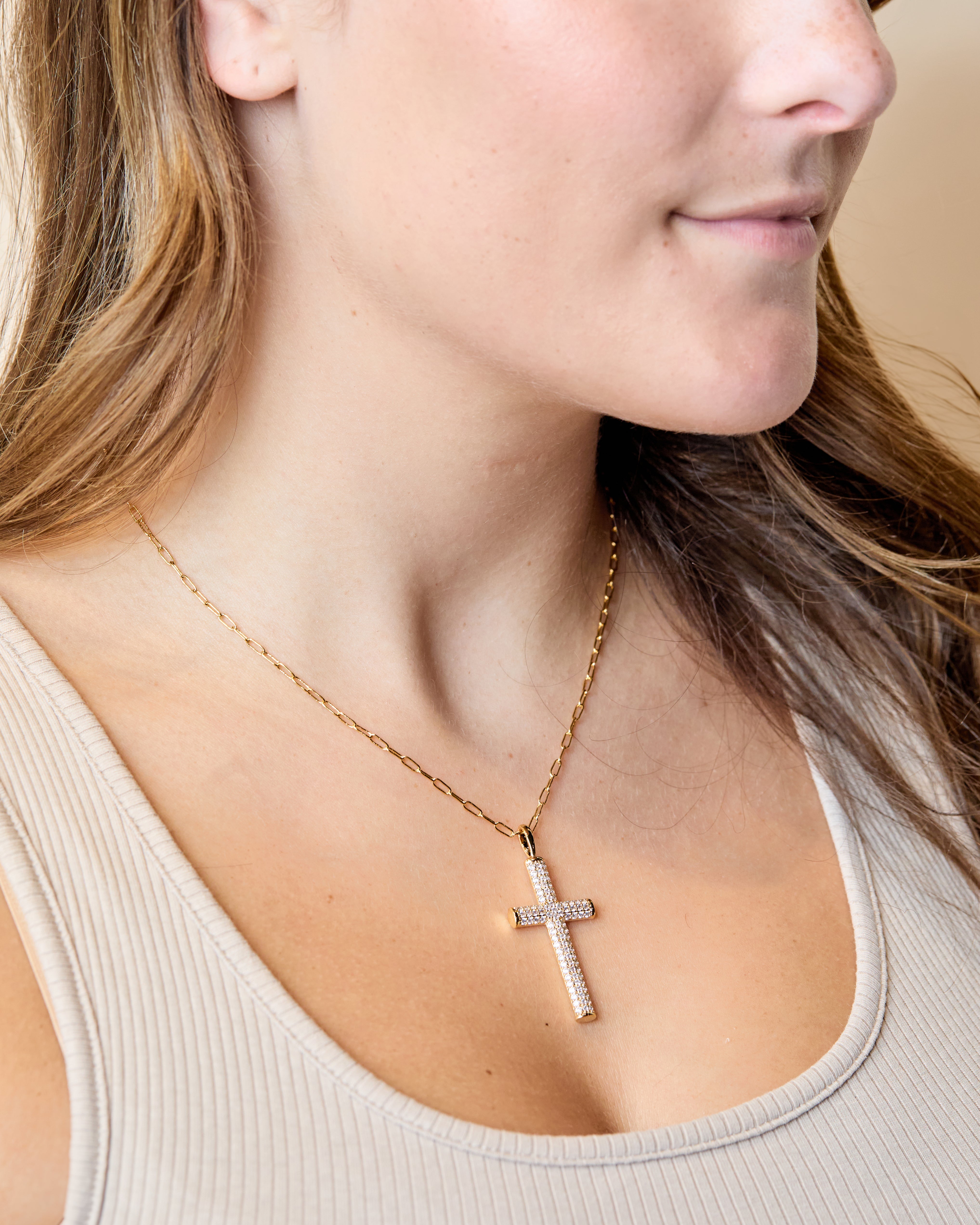 A gold chain necklace with a sparkling CZ-encrusted cross pendant worn by a woman.