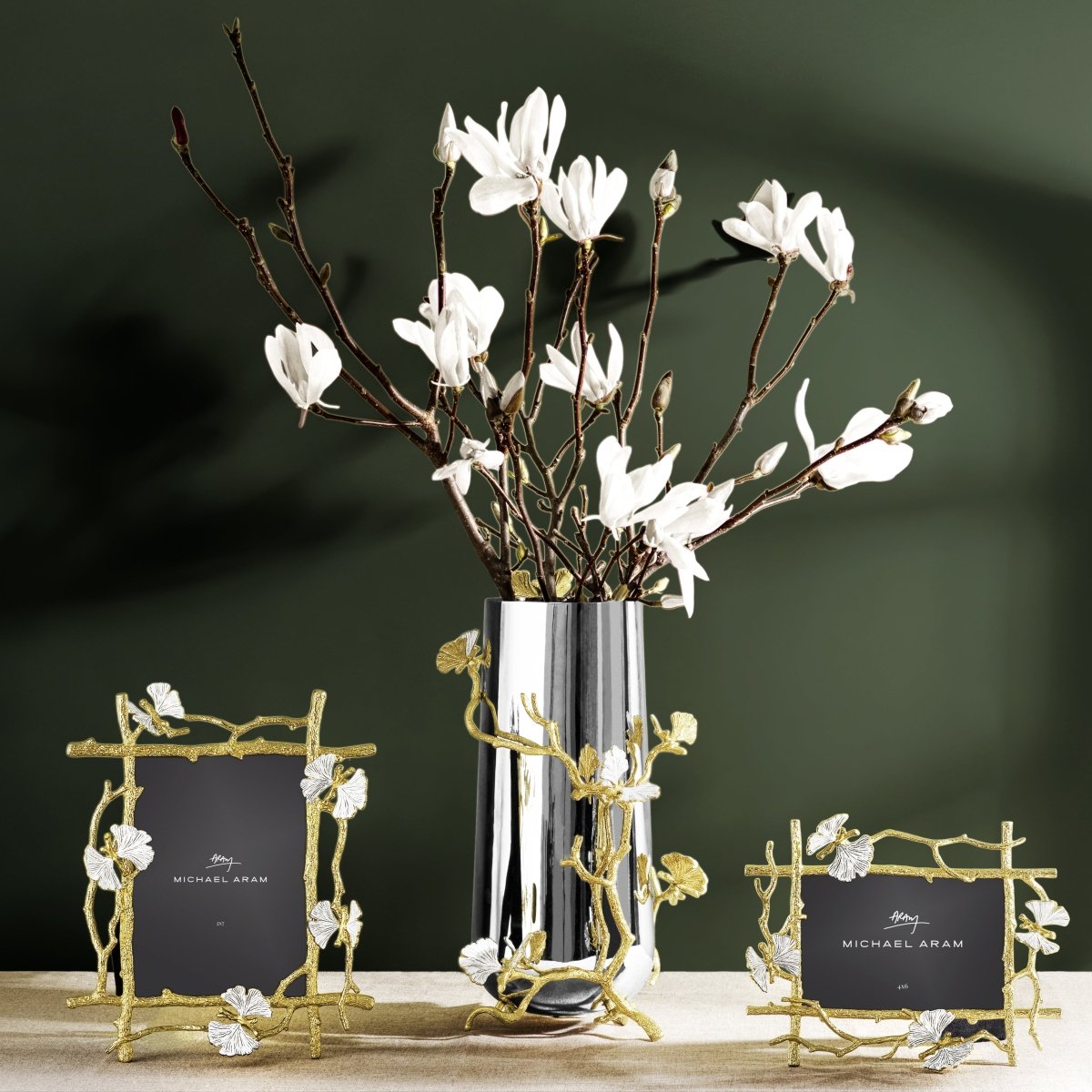 Two gold Butterfly Ginkgo picture frames and a matching silver vase with white magnolia branches.