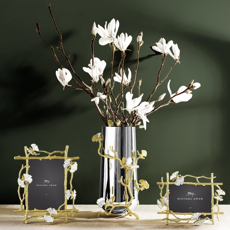 Two gold Butterfly Ginkgo picture frames and a matching silver vase with white magnolia branches.
