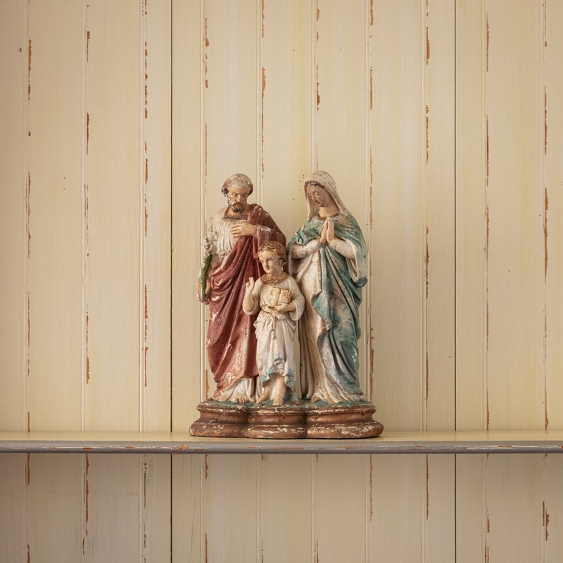 Aged resin Holy Family statue of Joseph, Mary, and child Jesus on a shelf.