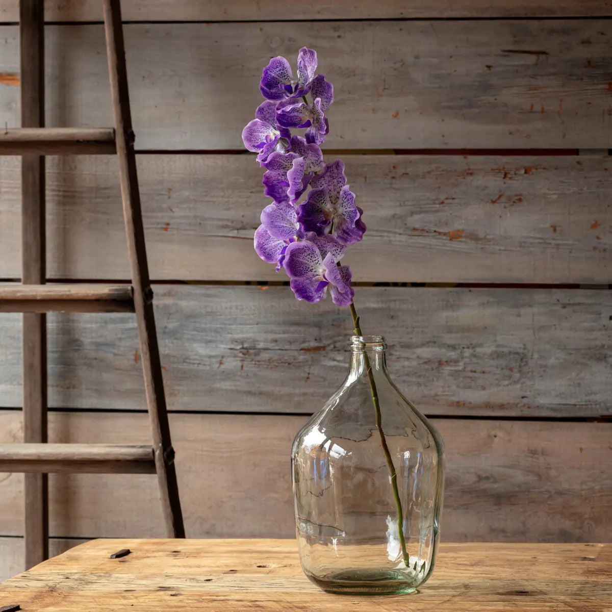 Vanda Orchid artificial flower arrangement in a clear glass vase with green foliage accents.