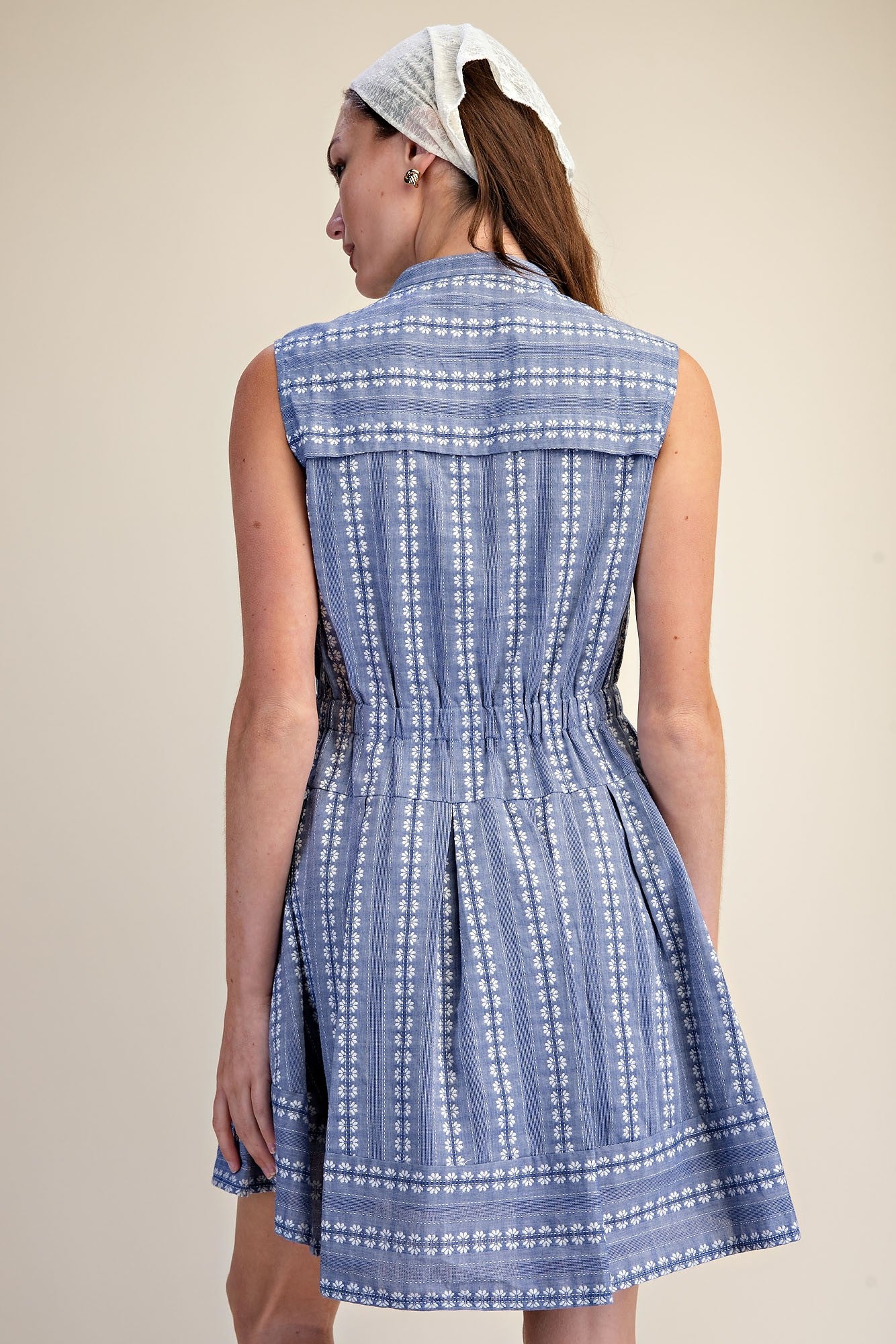 Back view of a sleeveless blue and white embroidered fit and flare shirt dress with cinched waist.