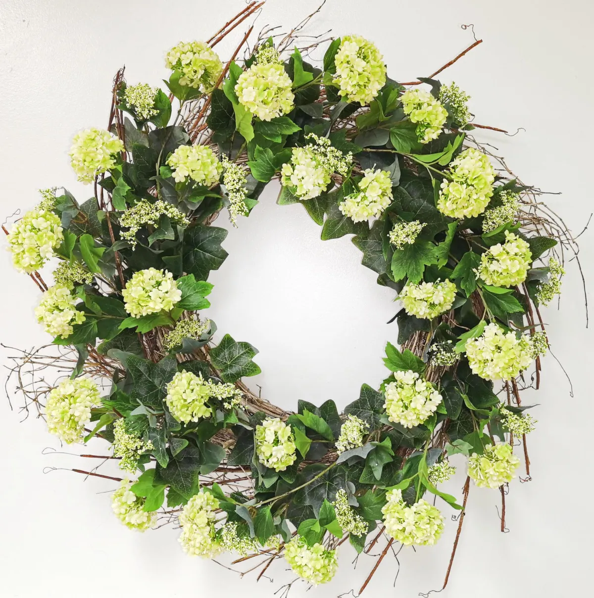 Green snowball wreath with natural pine branches arranged in a circular shape.