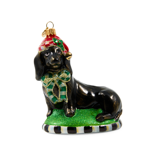 Holiday dachshund glass ornament wearing a red Santa hat and green plaid bow on a glittery base.