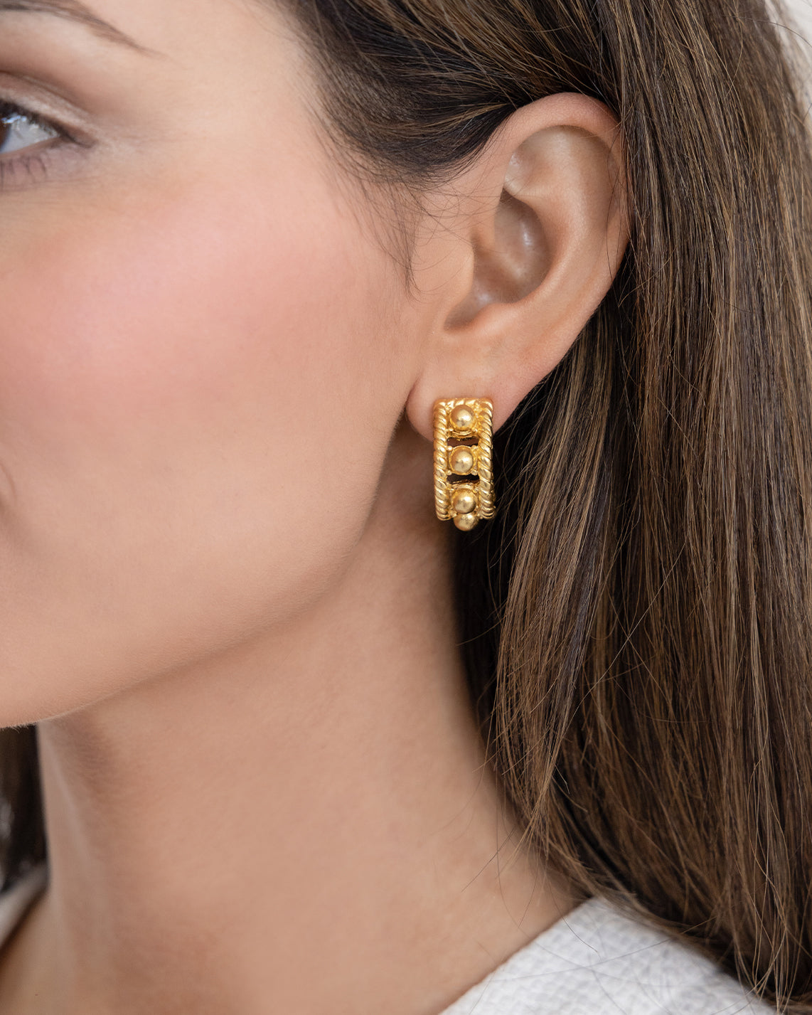 Close-up of a woman wearing a gold Capri Hoop earring with a textured, triple-beaded design.