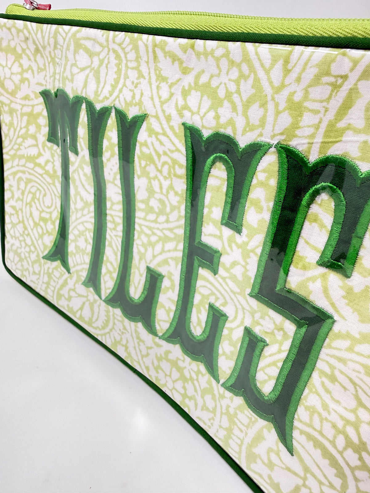 Close-up of a lime green paisley cosmetic bag with the word TILES in dark green applique.