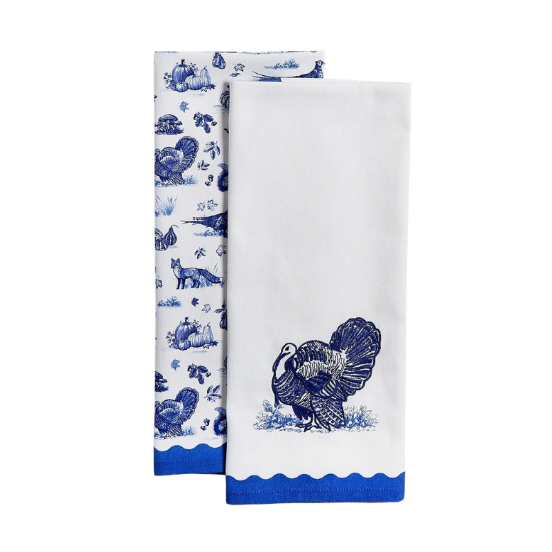 Two white dish towels with blue toile patterns featuring turkeys, foxes, and pumpkins.