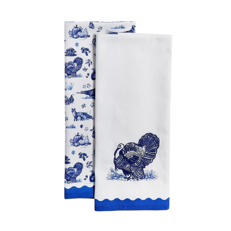 Two white dish towels with blue toile patterns featuring turkeys, foxes, and pumpkins.