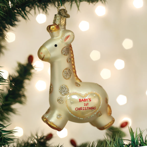 Baby's First Christmas Giraffe Ornament hanging on a tree with festive lights in the background.