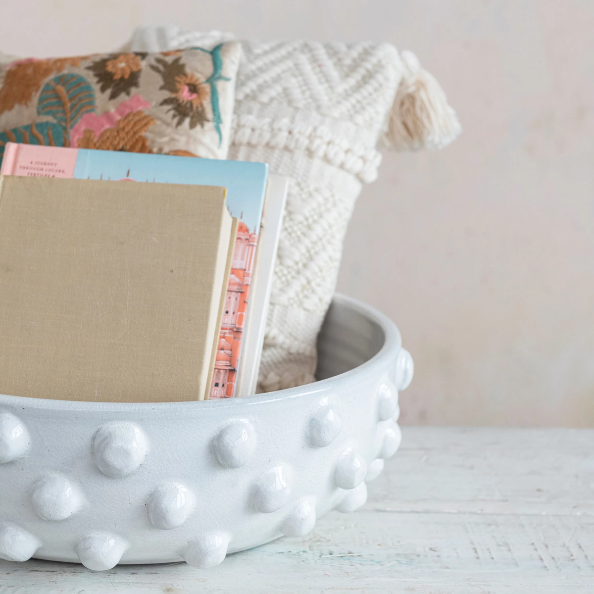 Round white terracotta bowl with a crackle glaze and raised dots, holding books and pillows.