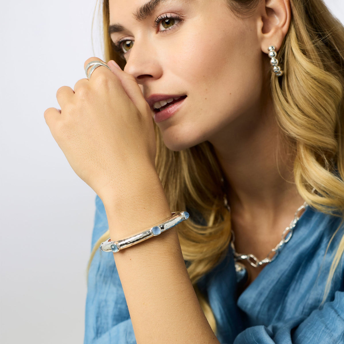 Woman wearing a Catalina Stone Hinge Bangle in silver with blue glass stones.