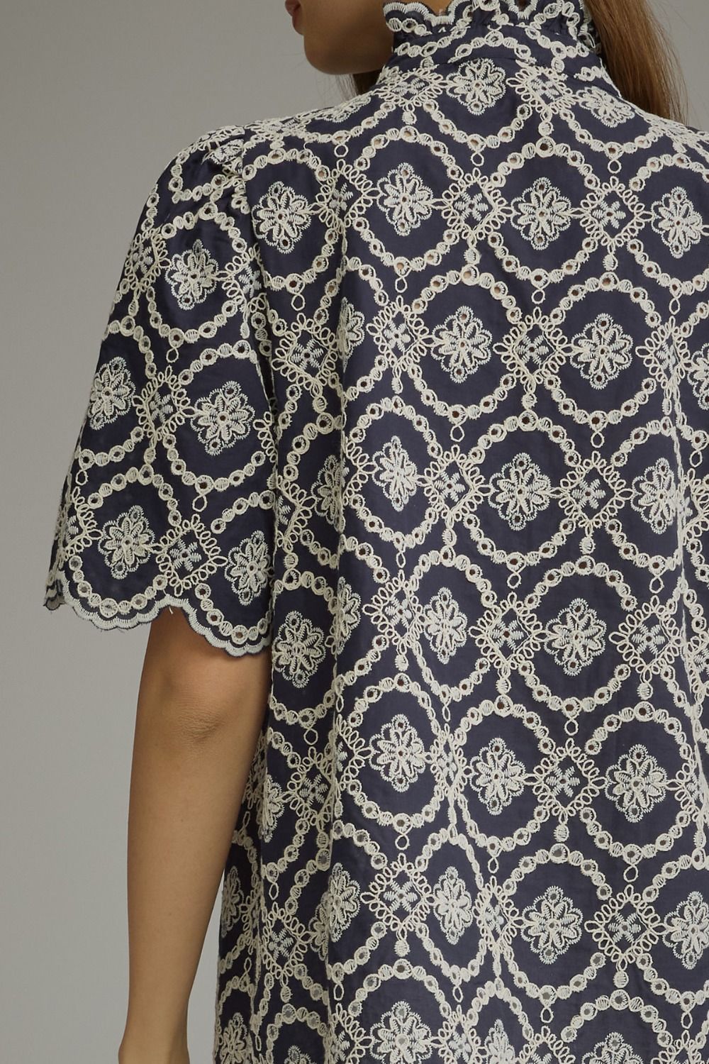 Back view of a navy Amalia top with white geometric embroidery, puff sleeves, and scalloped cuffs.