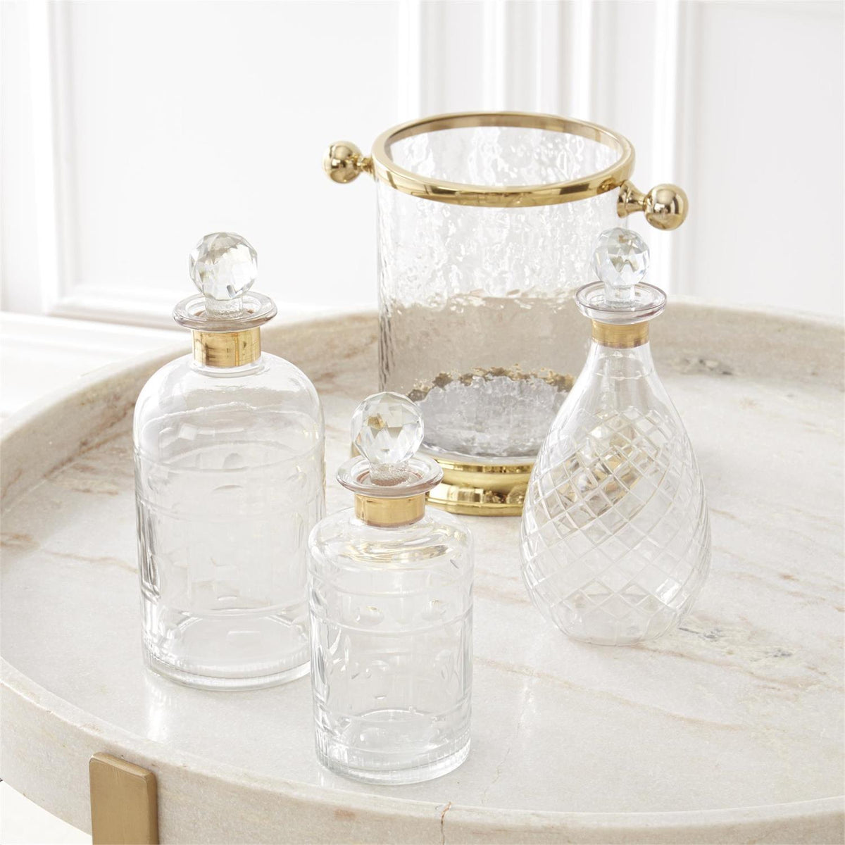 Three clear glass decanters with gold trim and crystal stoppers next to a matching glass ice bucket.