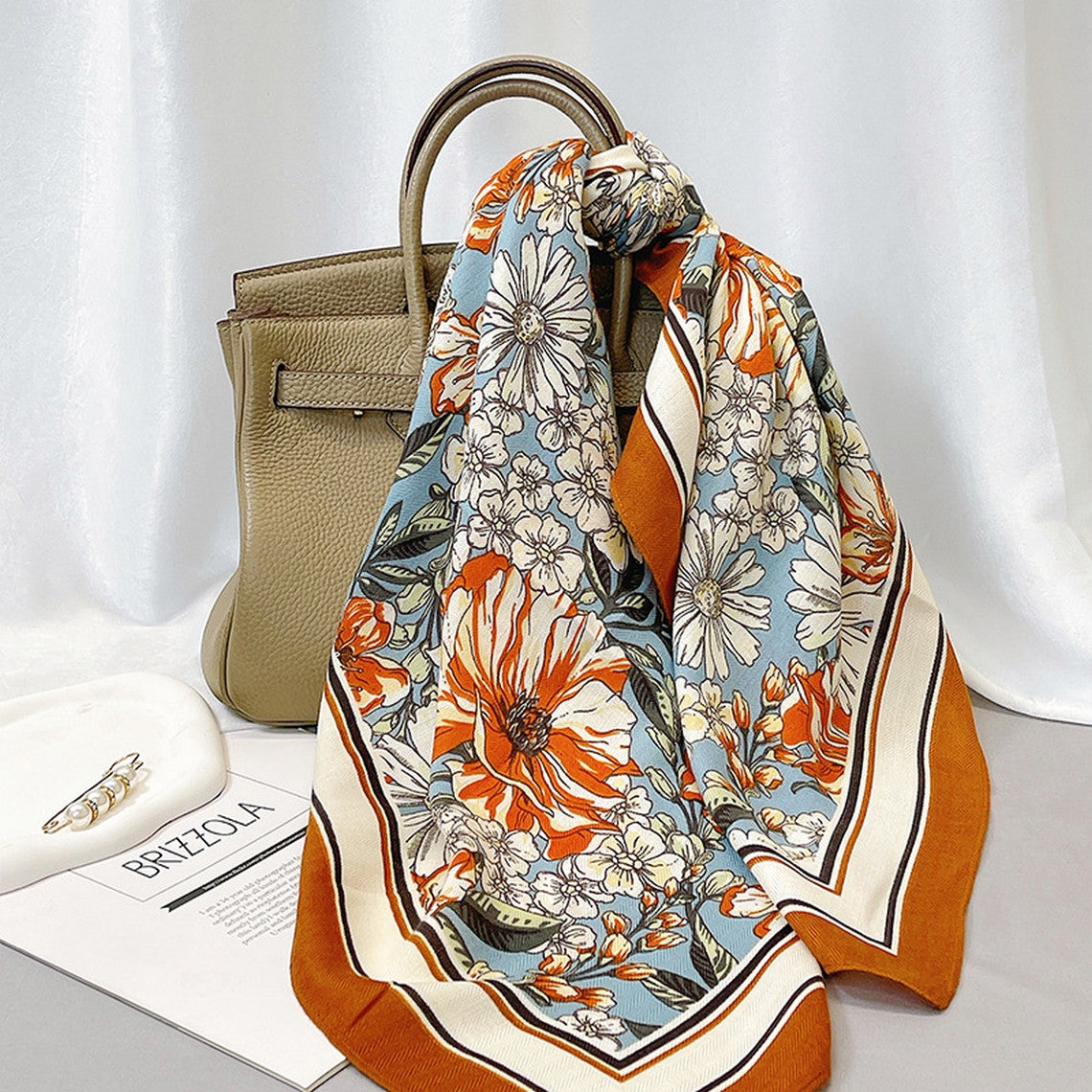 90cm floral velvet wool scarf in orange and blue with a large flower pattern tied to a tan handbag.