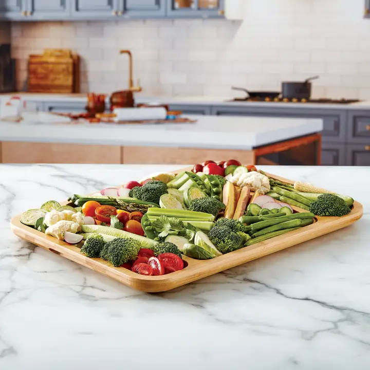 Bamboo charcuterie board with three compartments filled with fresh vegetables on a marble counter.