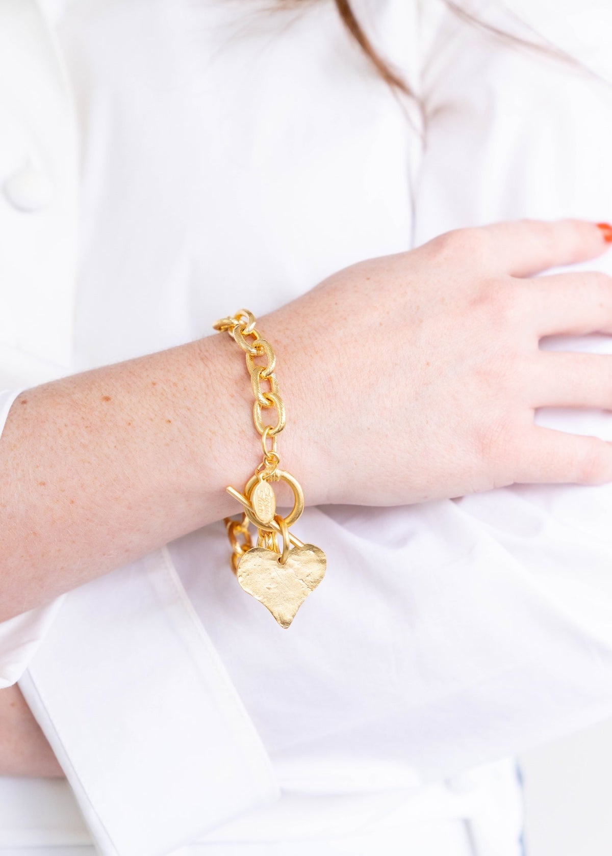 A person wearing a gold heart toggle bracelet with a hand-cast heart charm on a chunky link chain.