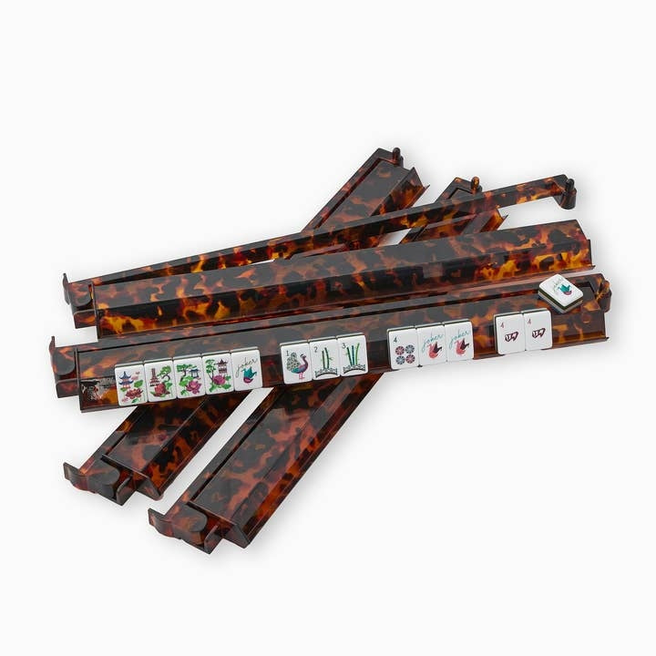 Four tortoise shell acrylic mahjong racks and pushers with tiles displayed on one rack.