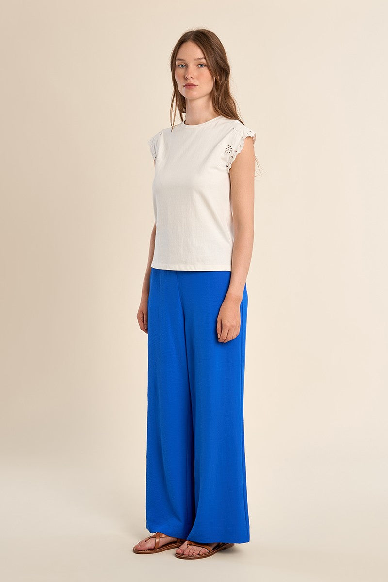 Woman wearing a white Madison knitted tee with embroidered short sleeves and blue wide-leg pants.