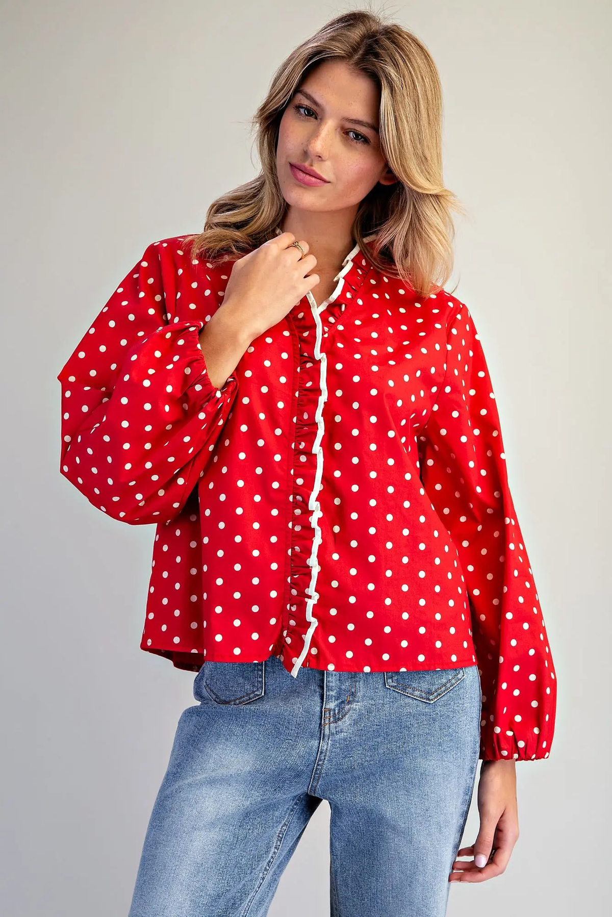 Woman wearing a red Blake Polka Dot Ruffle Button Down Blouse with long sleeves and blue jeans.