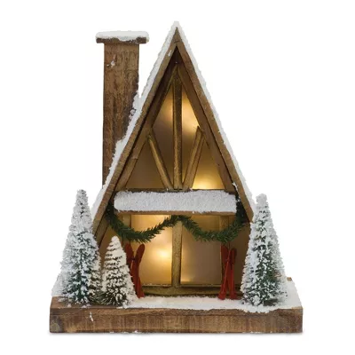 Lighted wooden A-frame ski lodge with snow-covered roof, chimney, pine trees, and red skis.
