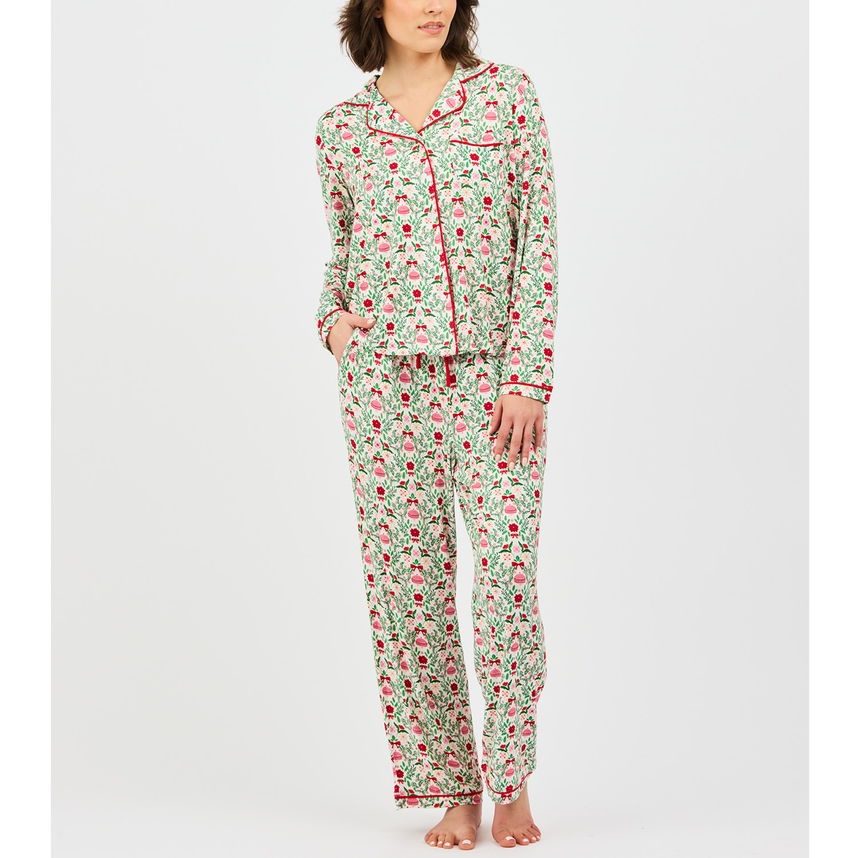 Woman wearing a long-sleeve pajama set with a red and green floral and ornament print.
