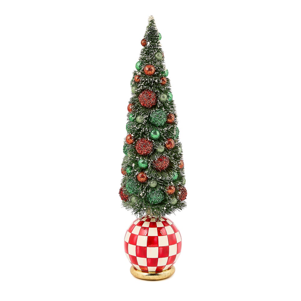 Frost-covered resin bottle brush tree with red and green baubles on a tabletop.