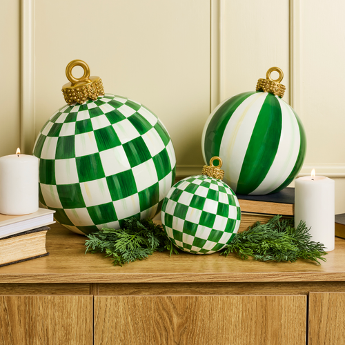 Three green and white patterned tabletop ornaments on a wooden surface with candles and greenery.
