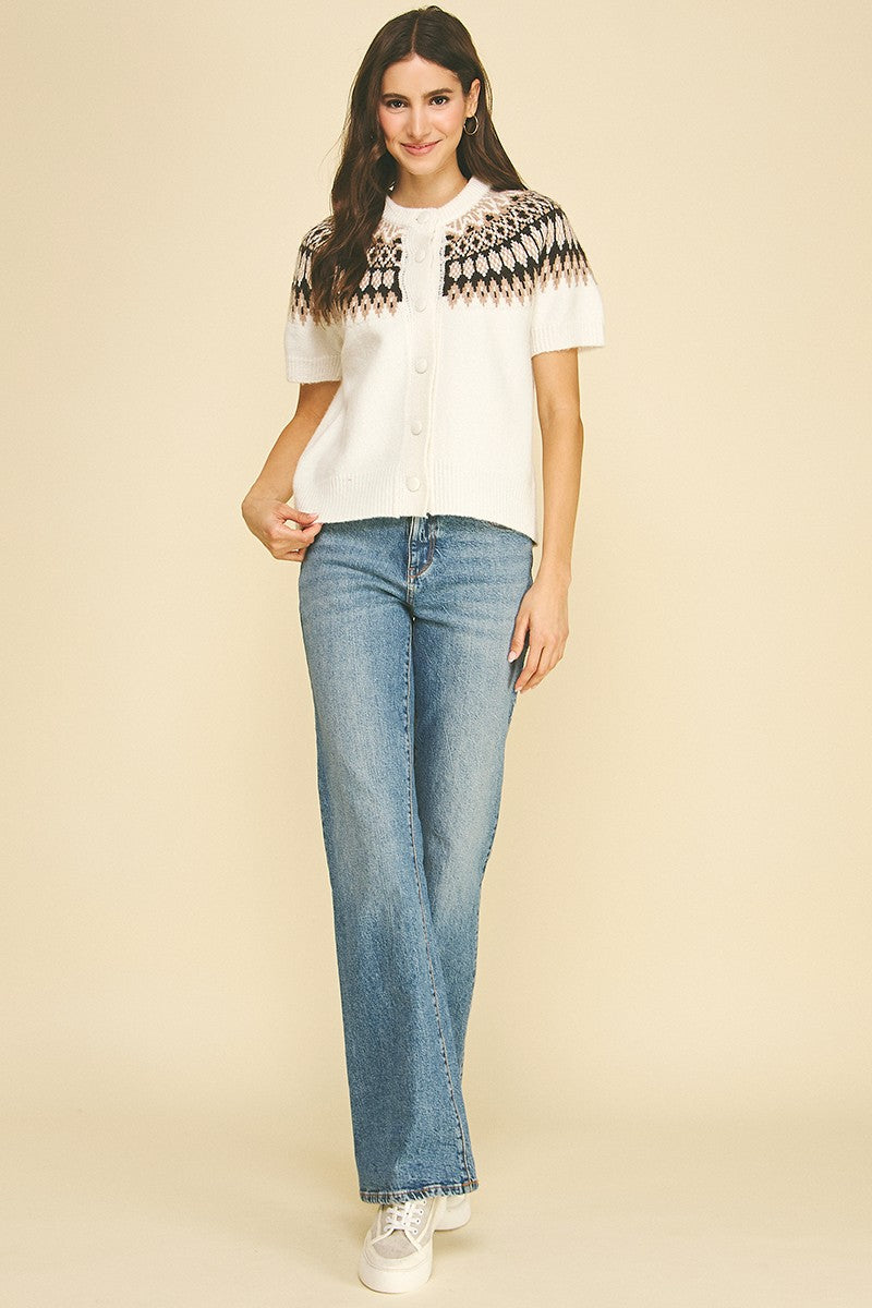 Woman wearing a white Jessica Nordic short sleeve knit cardigan with a fair isle pattern and jeans.
