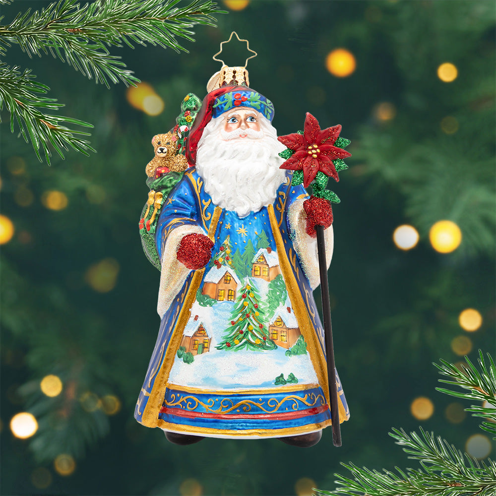 Father Christmas’ Eve glass ornament featuring Santa in a blue robe with a winter village scene.