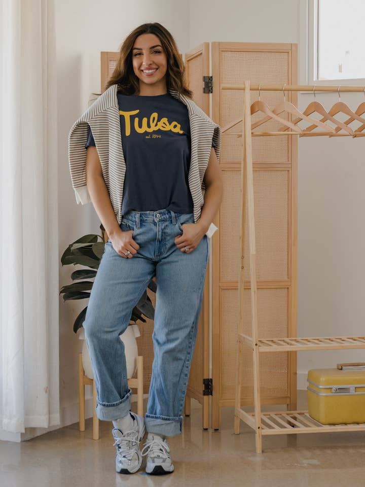 Woman wearing a navy Tulsa Hurricane Bold Script Ellie Heavyweight Tee with light wash jeans.