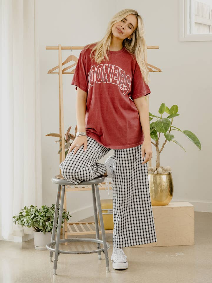 Woman wearing a maroon Athena OU Sooners Polka Dot Puff Ink CC Tee and gingham pants.