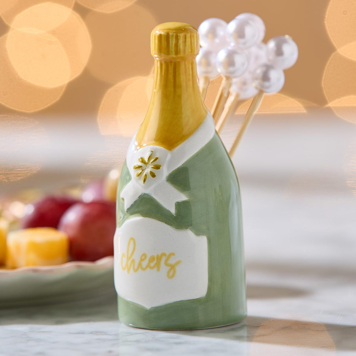 Ceramic champagne bottle pick holder with 'Cheers' label and pearl-topped cocktail picks.
