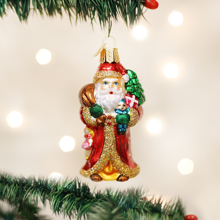 Father Christmas glass ornament holding a green tree and gifts, hanging on a Christmas tree branch.