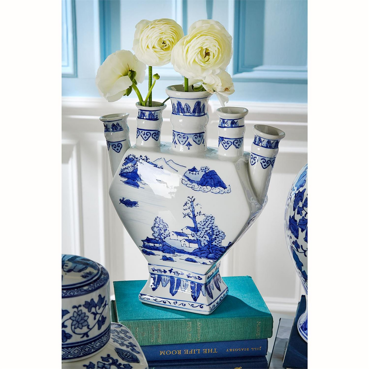 Canton ceramic blue and white multi-spout tulipiere vase with landscape scene on a stack of books.